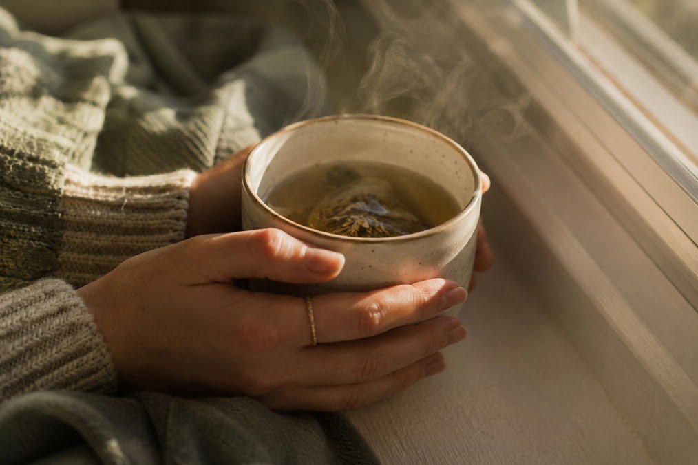 Two hands cradling a warm mug of tea by a sunlit window