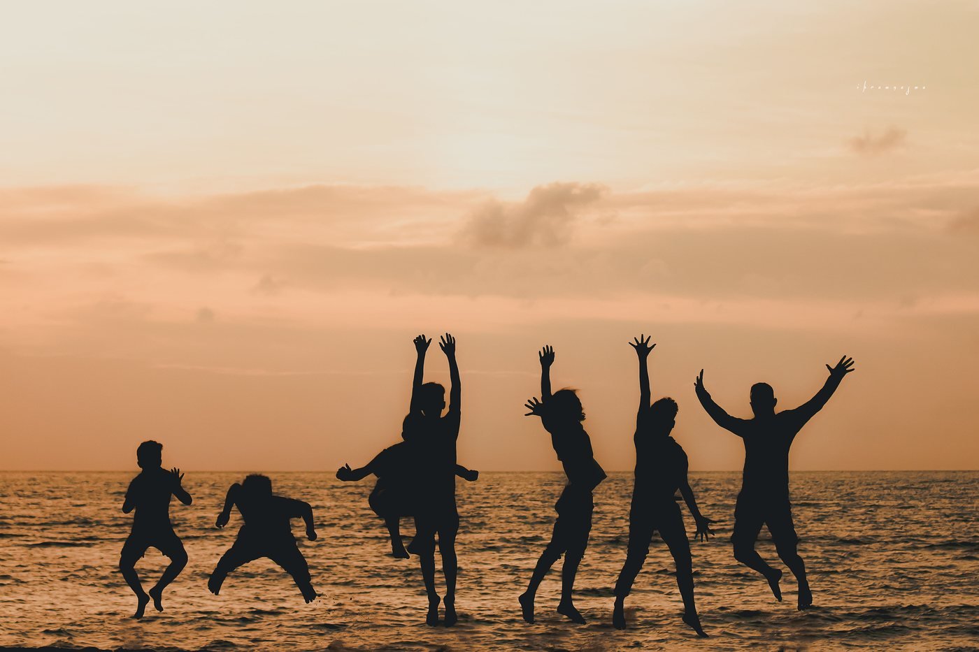 Silhouettes of a group of people leaping together on a beach at sunset