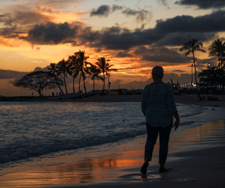 One person walking alone along a shoreline at sunset, palm trees on the horizon